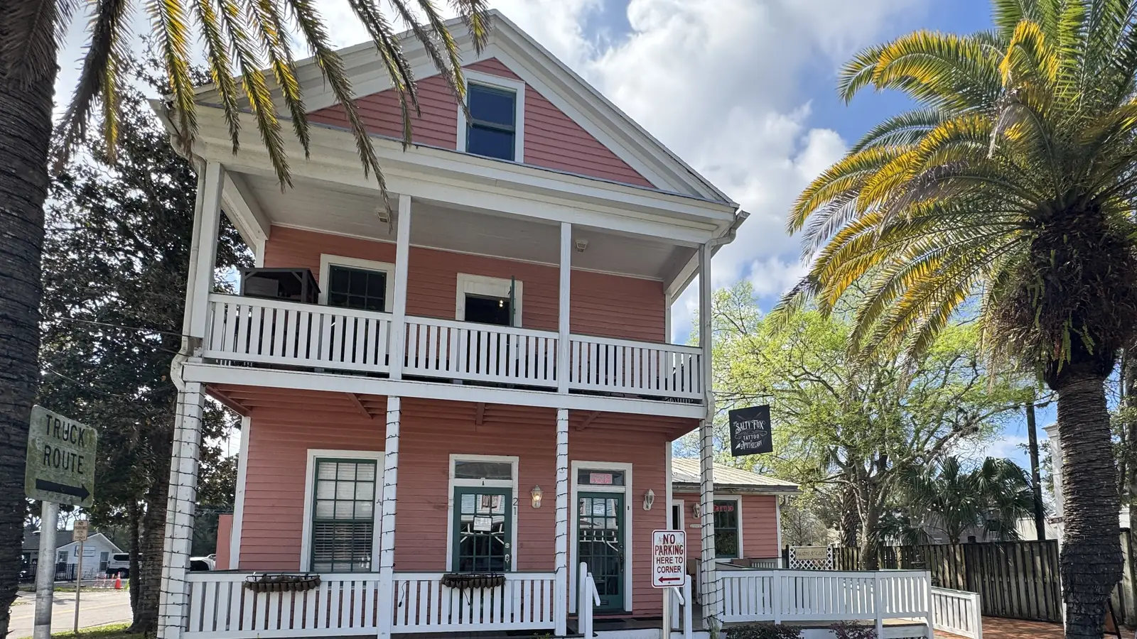 Garden Street Bistro's two-story coral building with white porches, framed by palm trees on South 3rd Street