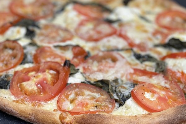 Thin-crust white pizza topped with fresh tomato slices and spinach